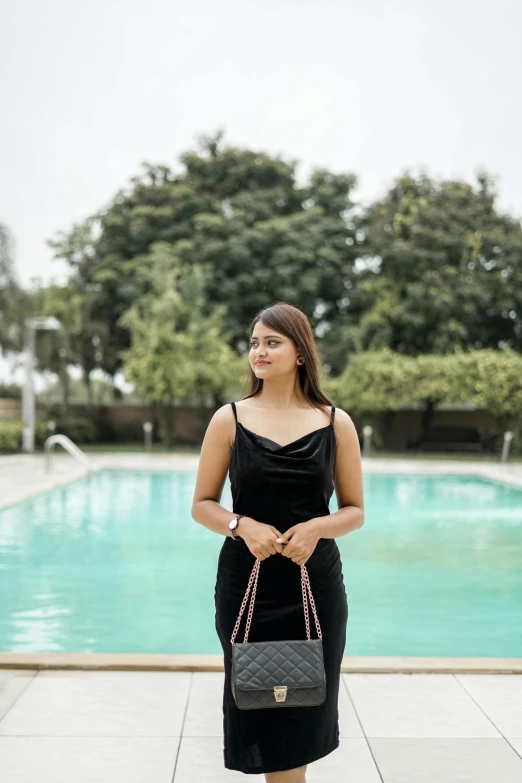 woman in black dress with her purse and smiling in front of the pool