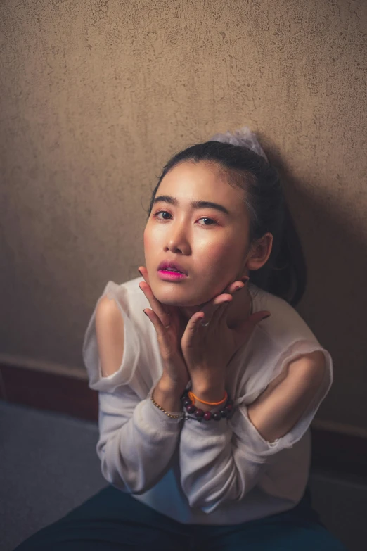 a woman sits against the wall while wearing a white blouse and necklace