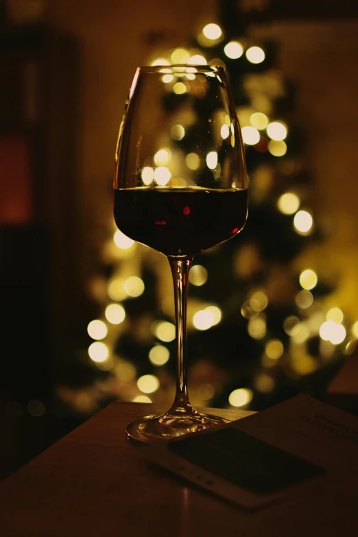 a glass of red wine sitting on top of a table next to a christmas tree