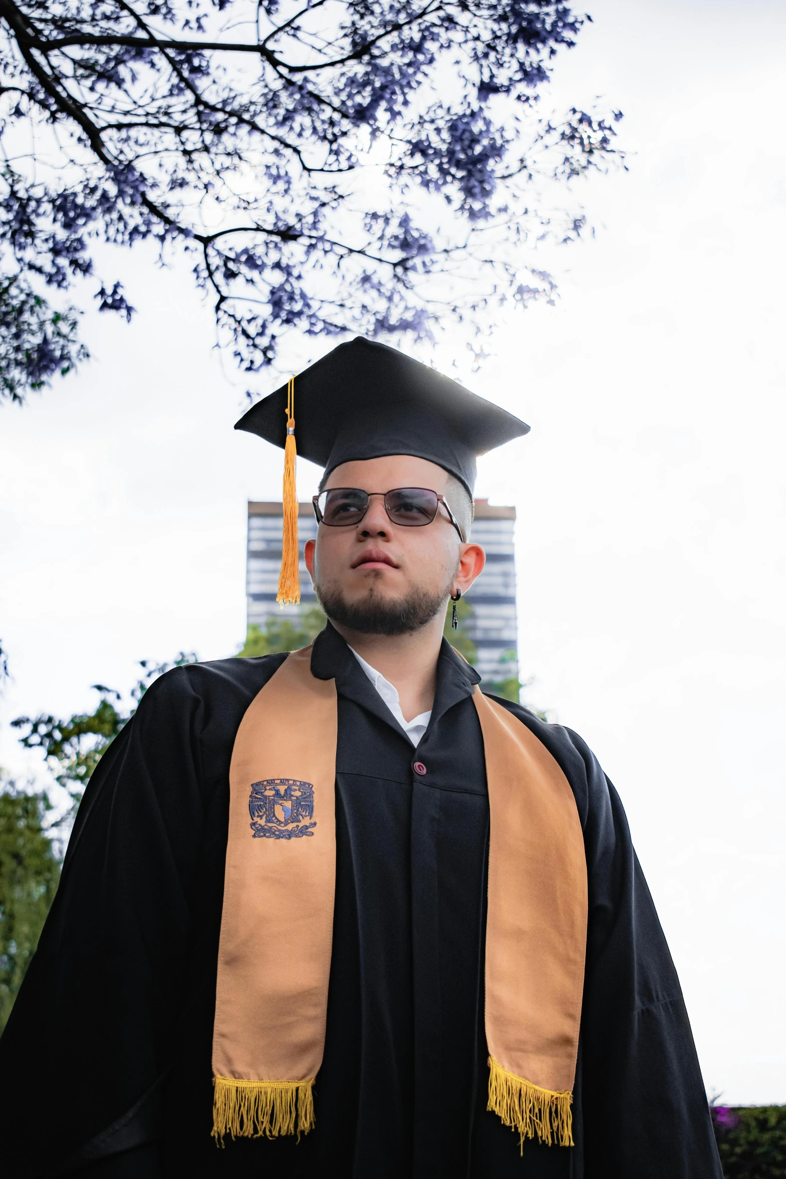 young man in cap, gown and stole posing in front of tree