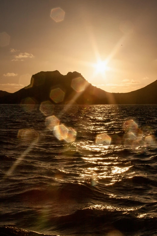 the sun shining brightly above mountains over a body of water