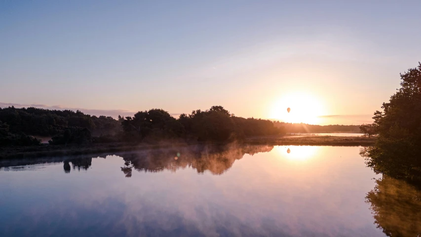 the sun is setting at the water's edge