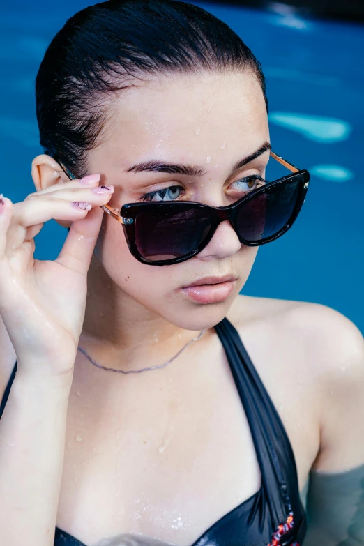 a woman in a swim suit putting her hand on her head and holding her sunglasses