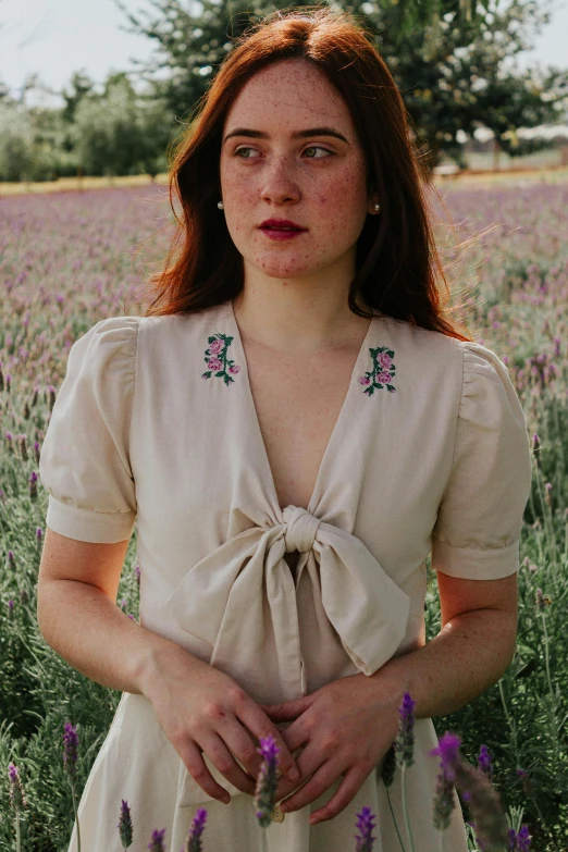 a woman standing in a field of flowers wearing a blouse with a tied around the shoulders