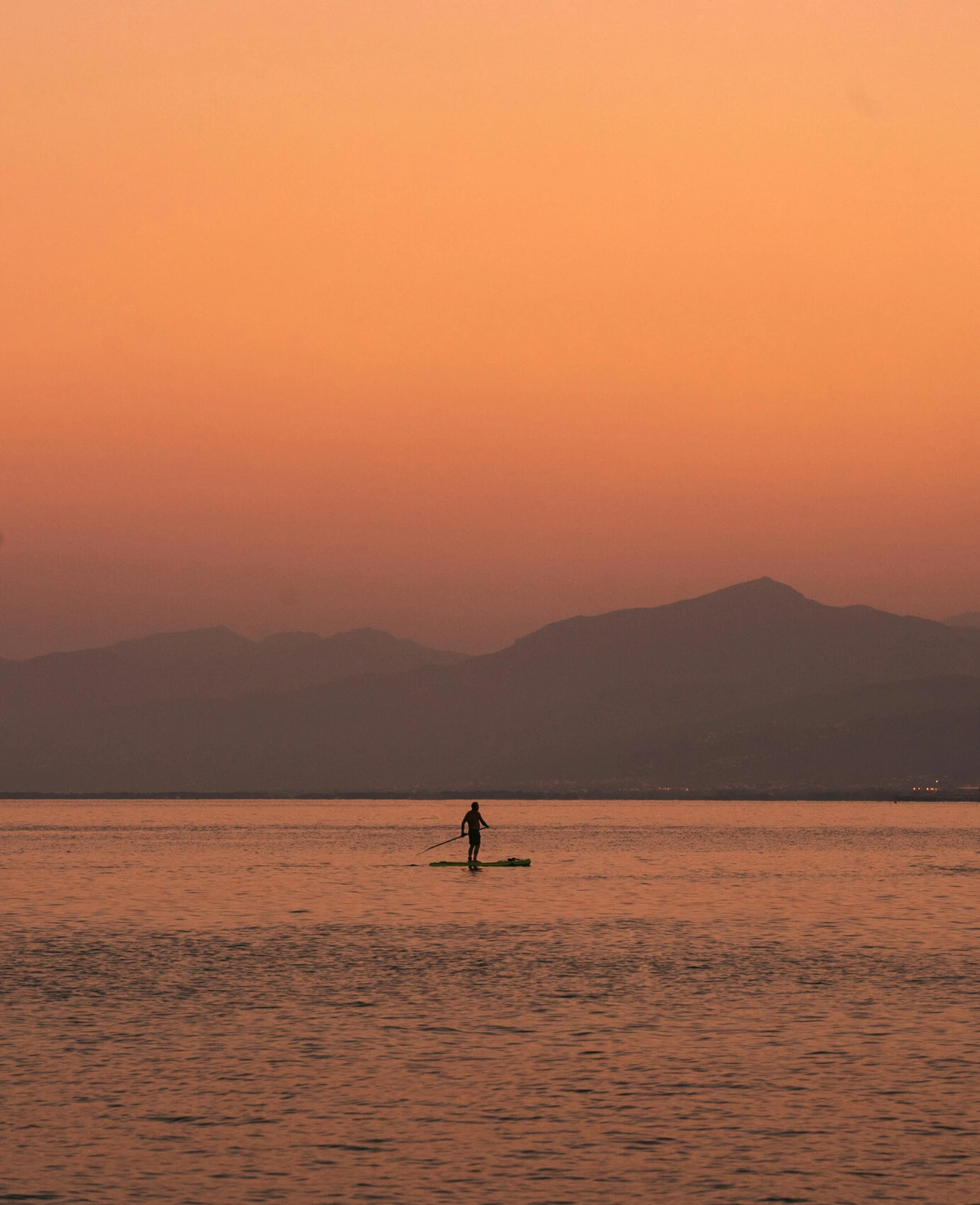 a person on surfboard on calm ocean at sunset