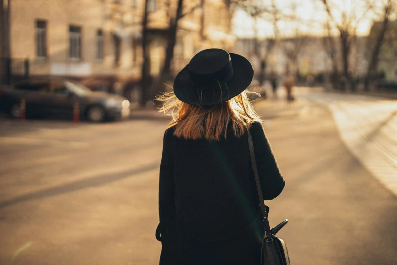 a woman in black coat and hat walking down street