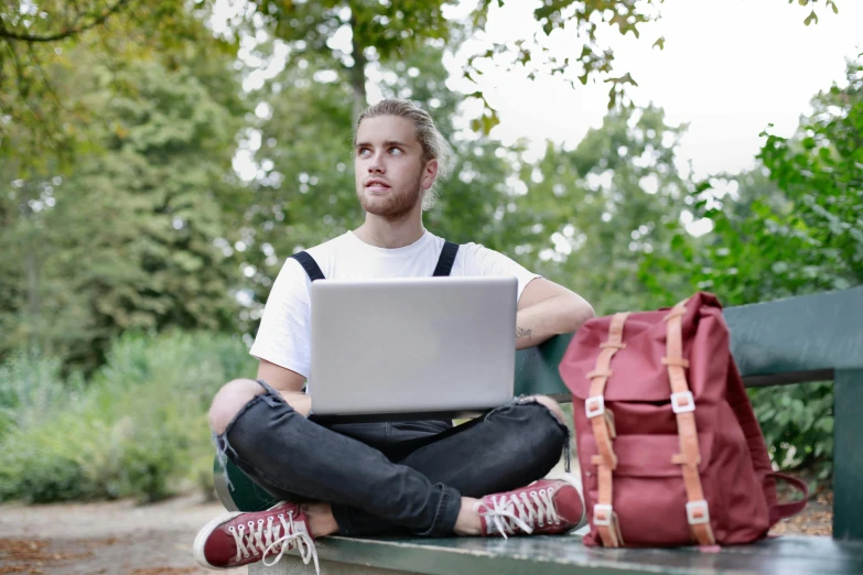 a man in suspenders sitting on a bench while using a laptop