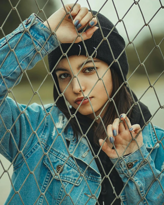 a woman in a beanie leaning on a fence