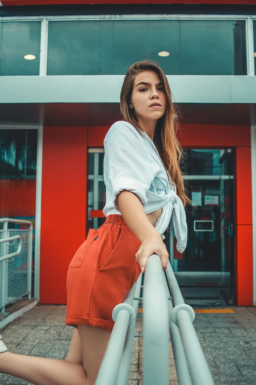 a girl in an orange shorts leaning on a metal fence