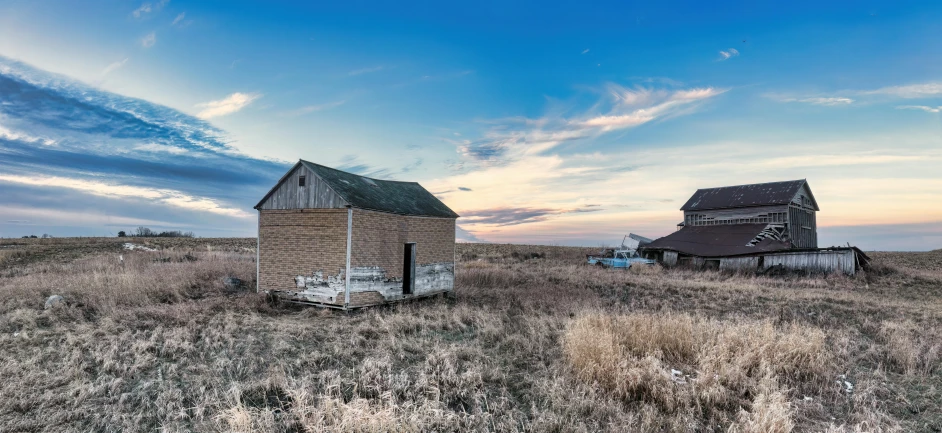 two barns on an open prairie during the day