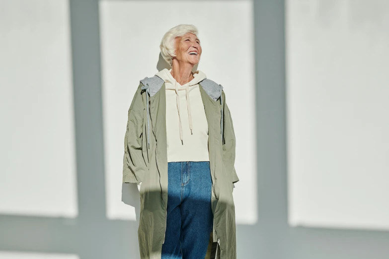 an older woman wearing a gray jacket and blue pants standing on a stage