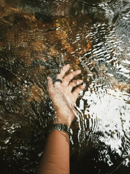 someone's hand reaching up to a rock in the water