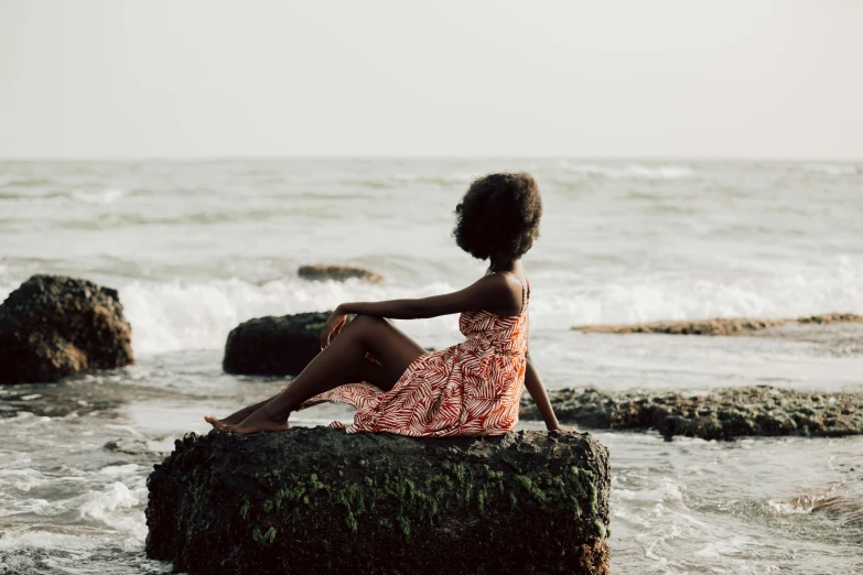 woman in a dress sitting on a rock looking out into the ocean