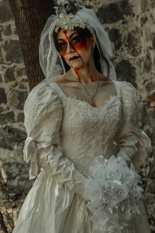 a bride with her makeup painted red, standing in front of a tree