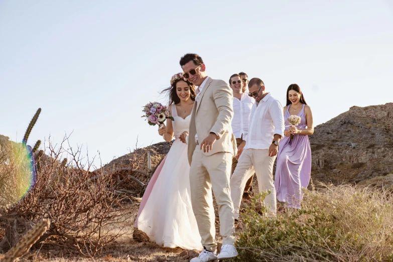 a couple walk through an arid area with their wedding party behind them