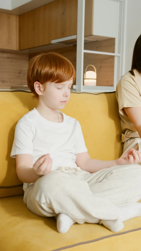 a little boy sits on a couch while his mother looks at soing