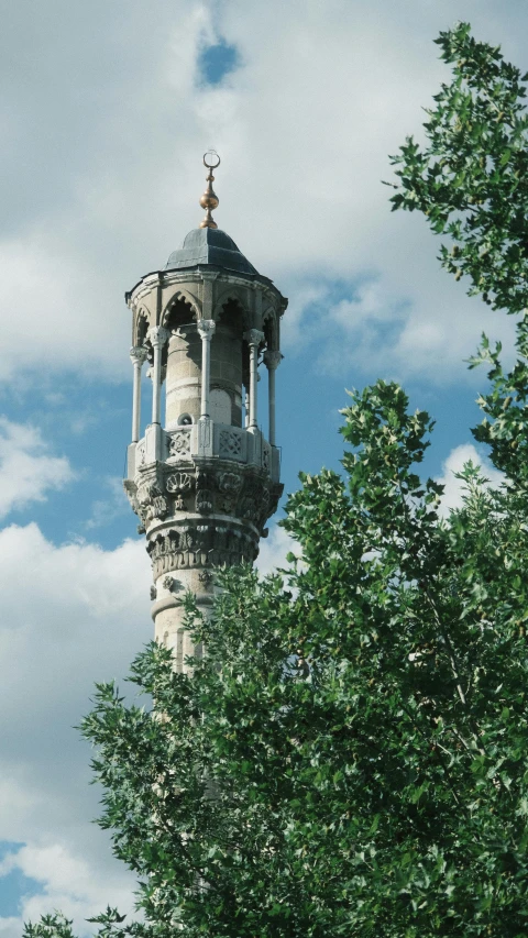 a clock tower near a tree and clouds