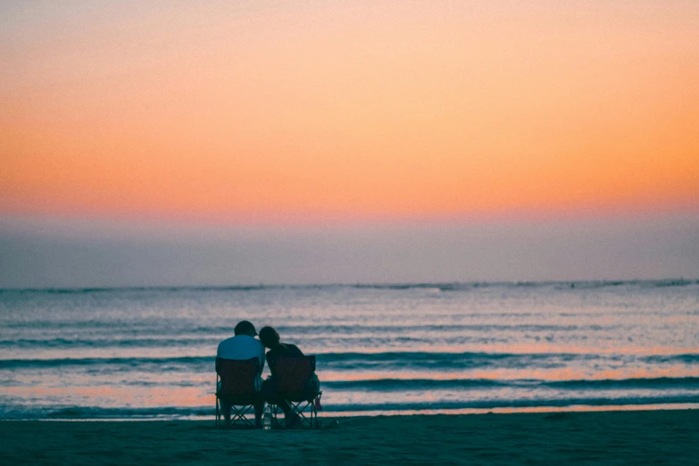 two people sitting on an umbrella by the water