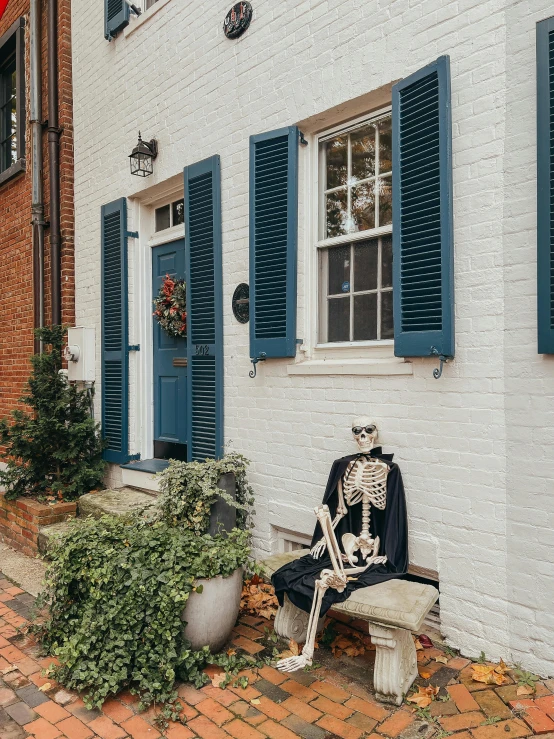 a skeleton sitting on a bench outside of a building