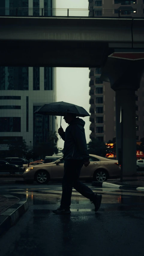 a man walks with an umbrella under an overpass
