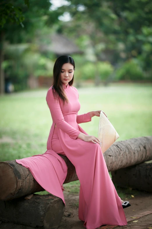 an attractive asian woman in pink sitting on a log