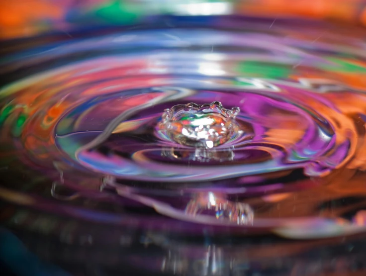 a droplet sitting in the middle of a colorful liquid
