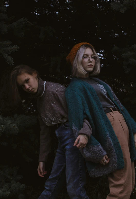 two young women dressed in sweaters and jeans walking down the street