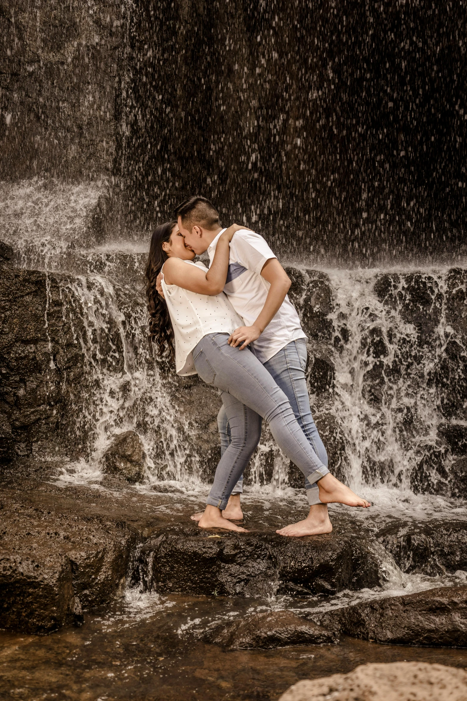 a man and a woman kissing in front of a waterfall