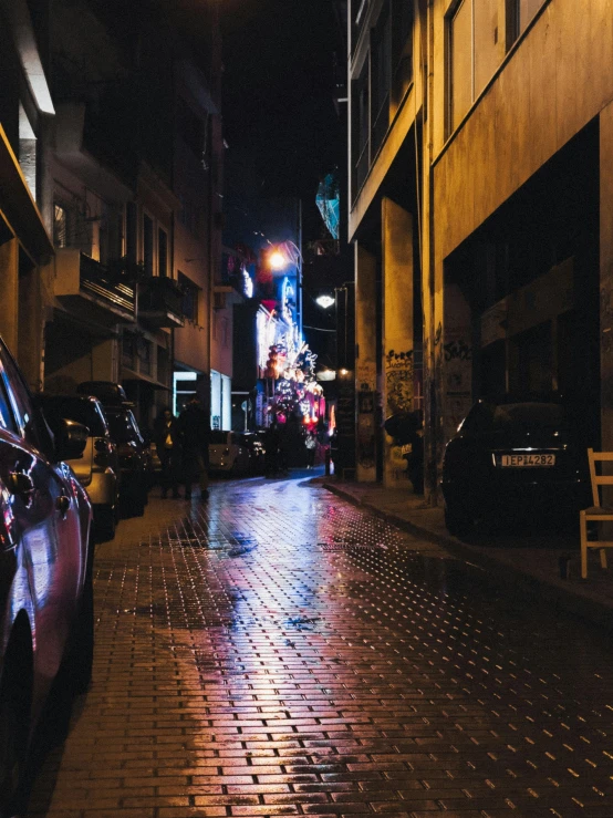 a dark street with parked cars and people in the distance