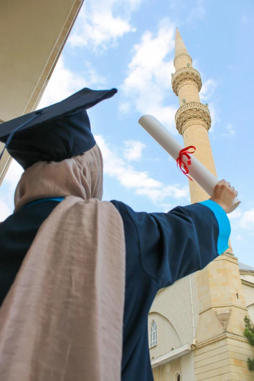 a person in a blue graduation outfit holds up a white and red tassel