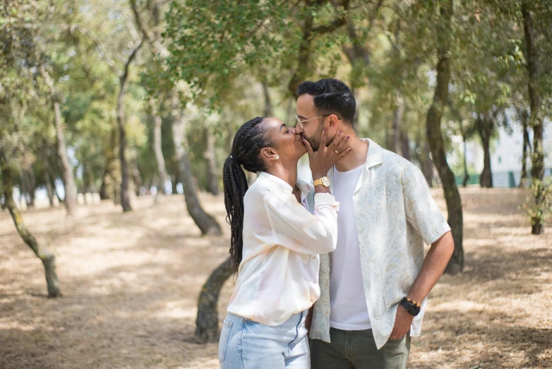 a woman kisses her man next to the trees