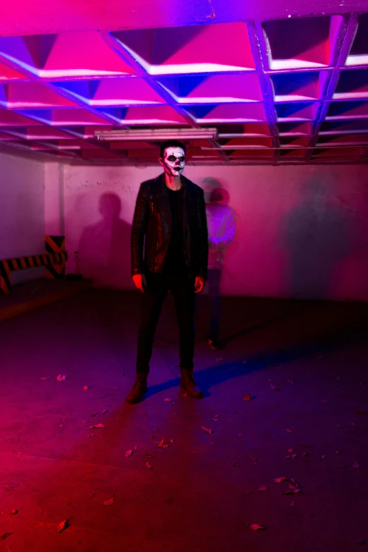 a man in white makeup and devil make up standing next to a purple background