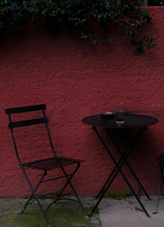 a pair of folding chairs and a small table sit next to a red wall