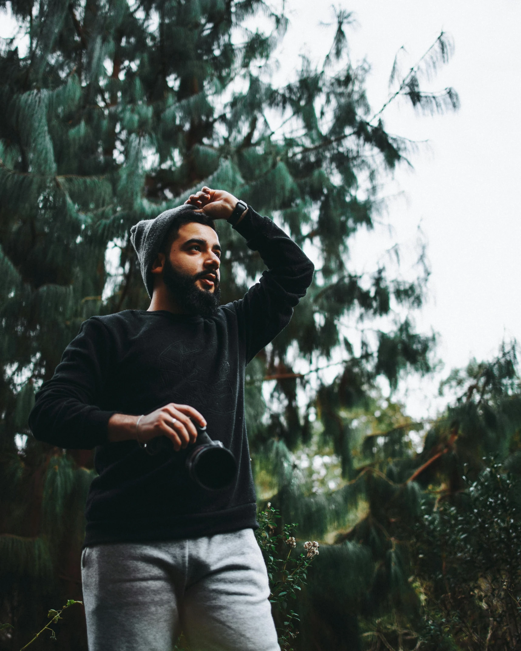 a man standing in the woods and staring at soing with one hand on his head