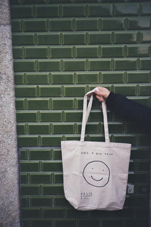 a person holds up a tote bag against a wall