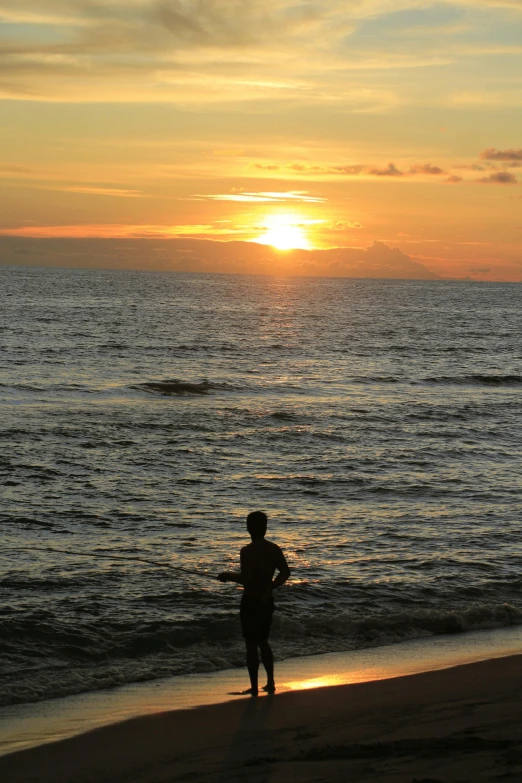 a person standing on the shore of a beach watching the sun set