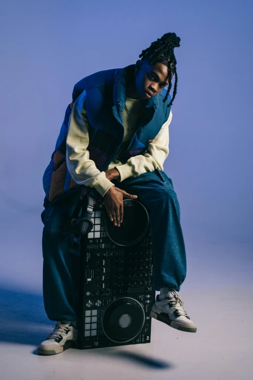 young man sitting on top of electronic equipment against a blue background