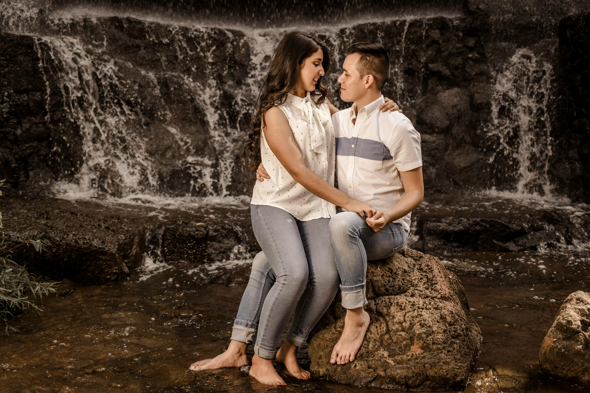 a man and woman sit together in front of a waterfall