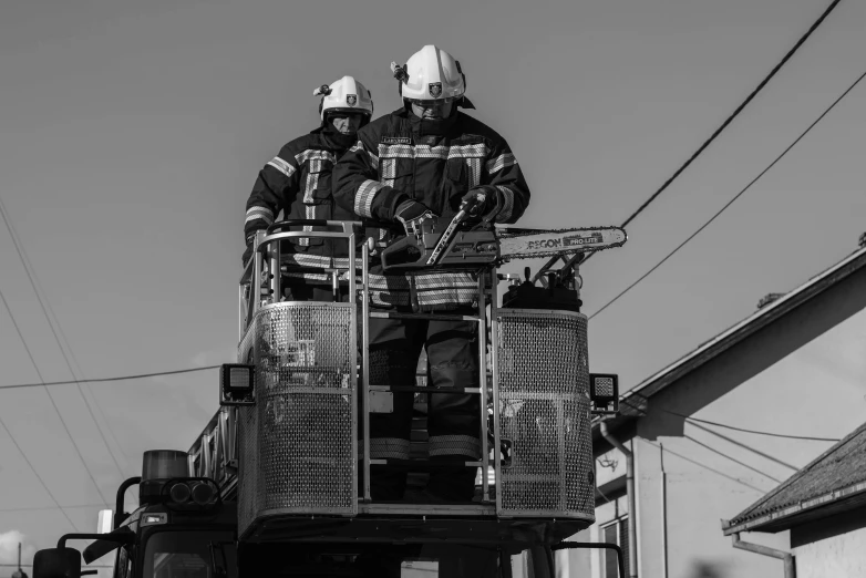 two fire fighters in firefighter uniforms standing on top of a vehicle