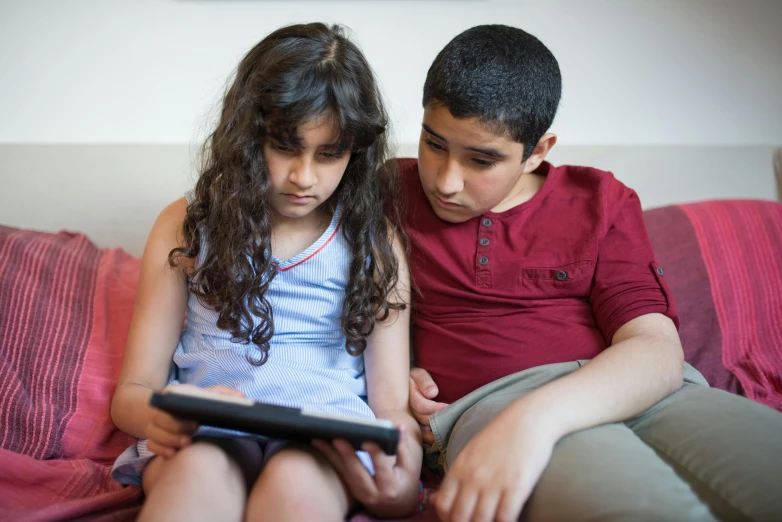 a boy and girl sitting on top of each other using a tablet