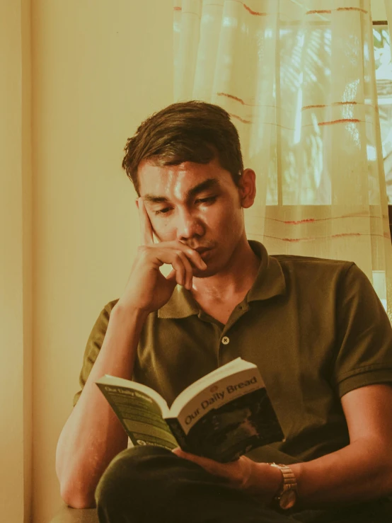 a young man sitting in a chair holding an open book