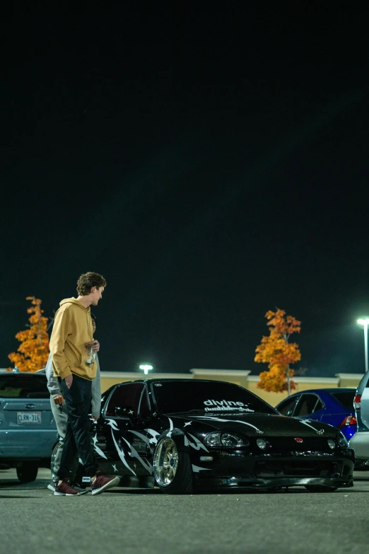 two boys standing next to each other next to a black car