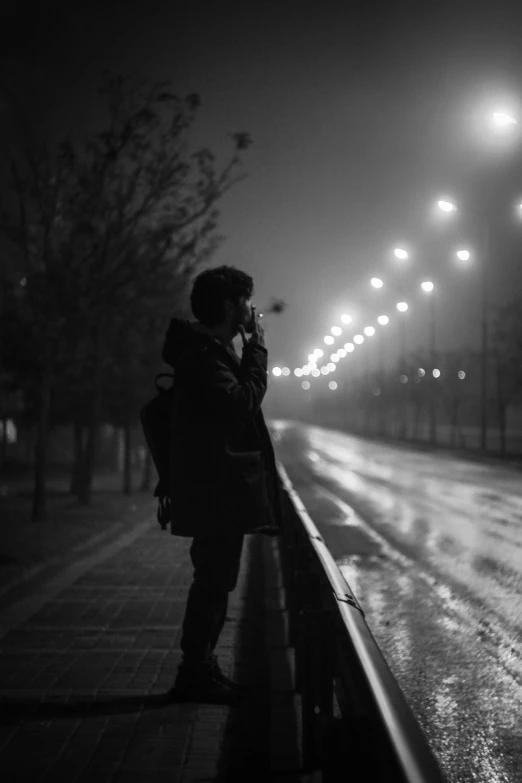 a man standing on a wet sidewalk at night using his cell phone