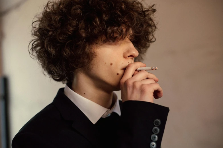 young man with curly hair and jacket smoking cigarette