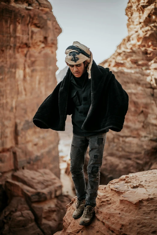 man wearing all black outfit while standing on rock by canyon