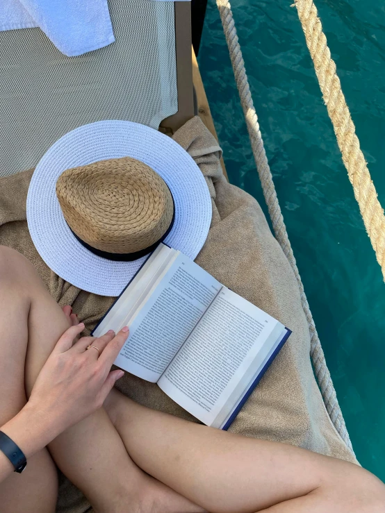 a girl with no pants sitting beside a swimming pool reading a book