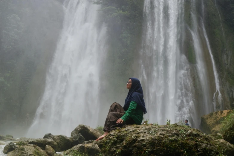 two people on a large rock with a waterfall in the background