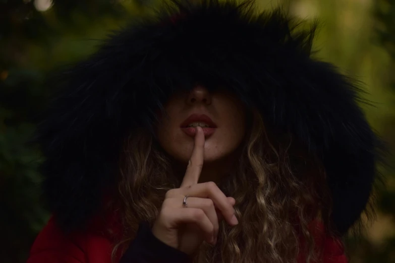 the woman has long hair and red coat over her head, finger to her lips