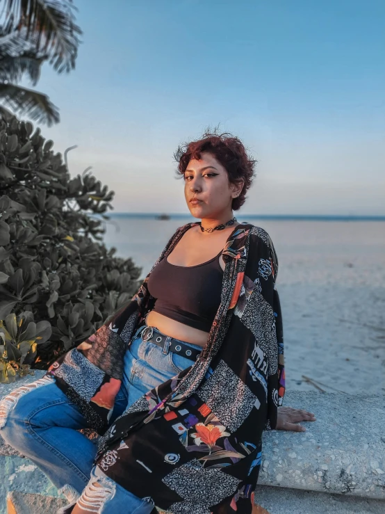 a woman in a dress sitting on a rock by the ocean