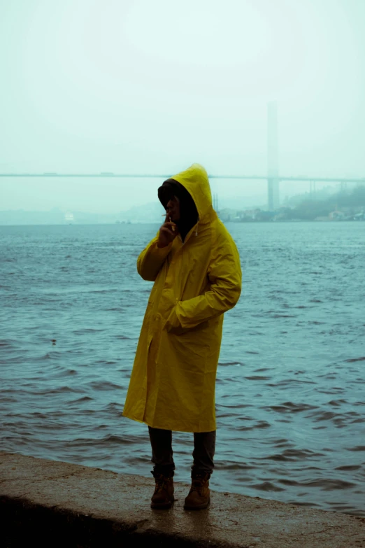 a man in a raincoat on the phone by the water